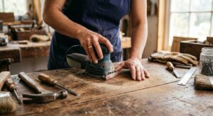 A high-quality, editorial-style close-up of a person’s hands professionally sanding a vintage wooden